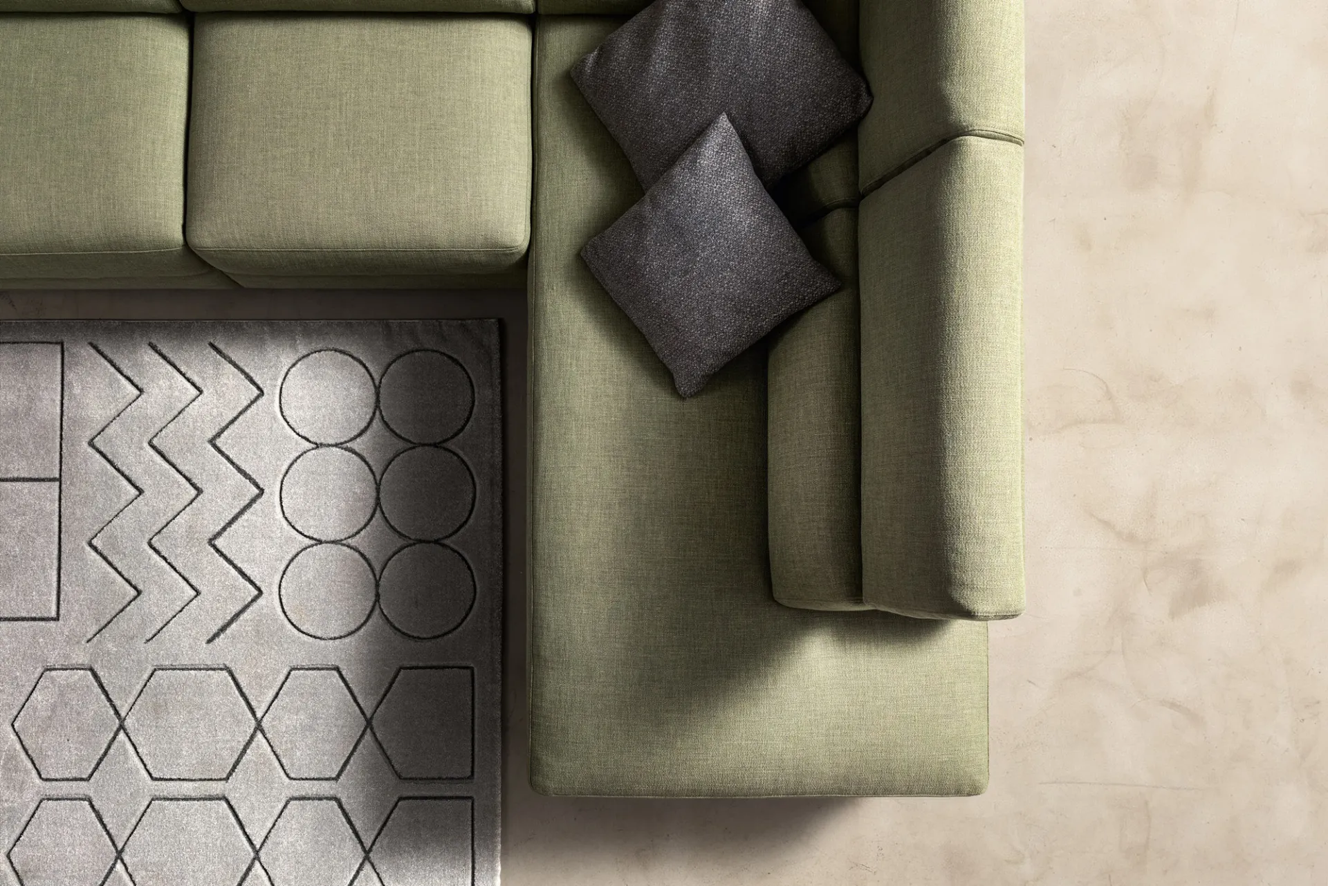 Divano Space Look Samoa verde visto dall'alto, con cuscino grigio e tappeto geometrico
