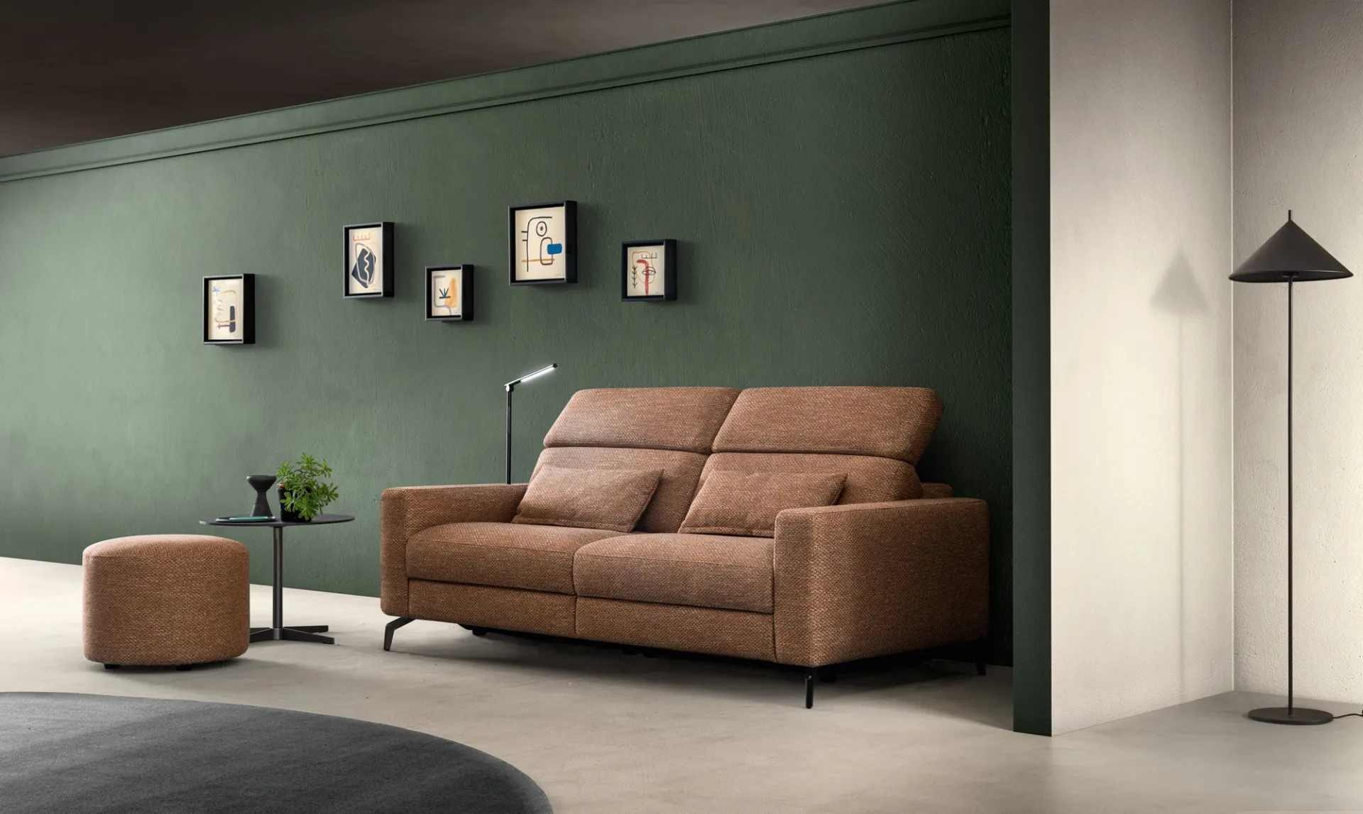 Divano Space Speed Samoa terracotta a due posti con pouf, davanti a una parete verde