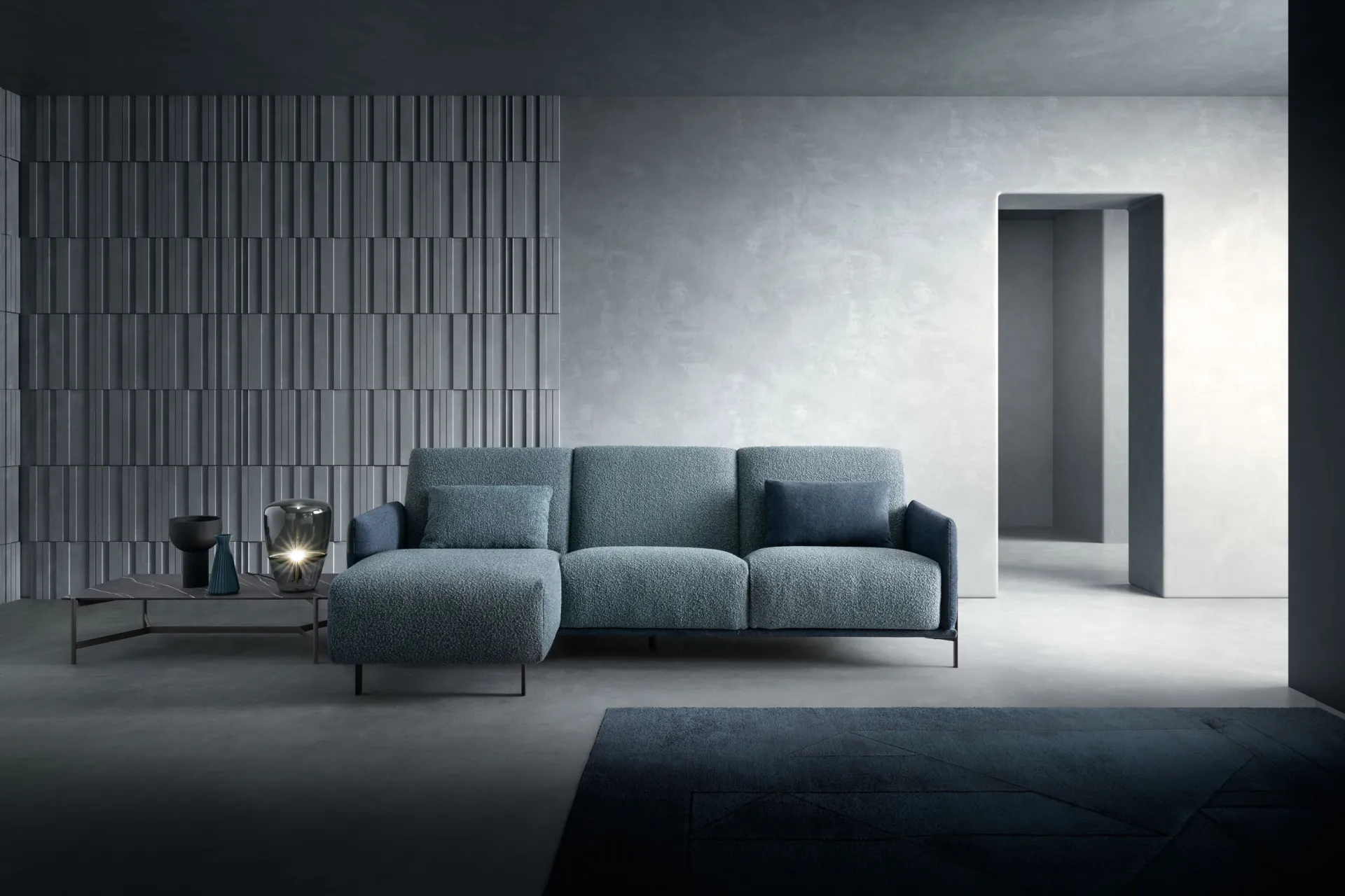 Divano Blank Samoa azzurro polvere con chaise longue e piede in metallo scuro, in un ambiente grigio blu