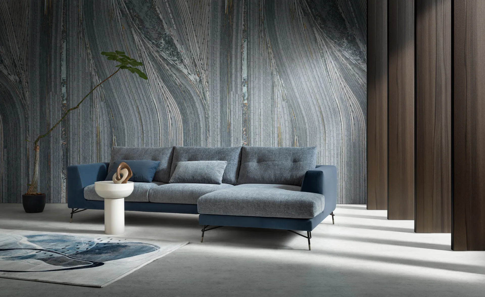 Divano Dafne Samoa con penisola in due tessuti, azzurro e blu, davanti a una parete decorata