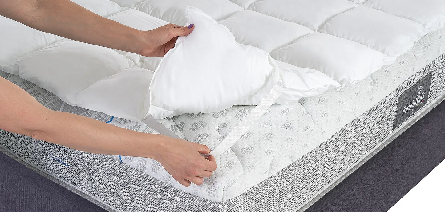 Angolo del Topper Essenziale Magniflex sollevato, con le mani che fissano l'elastico