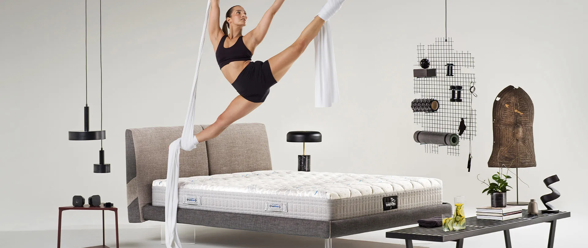 Materasso MagniStretch 10 Magniflex su letto imbottito grigio, con un'acrobata sospesa ai tessuti aerei