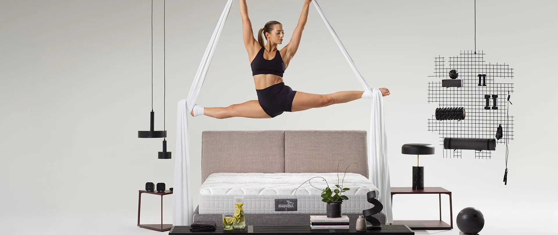 Materasso MagniStretch Magniflex su letto con testiera in tessuto, acrobata in spaccata sopra il letto