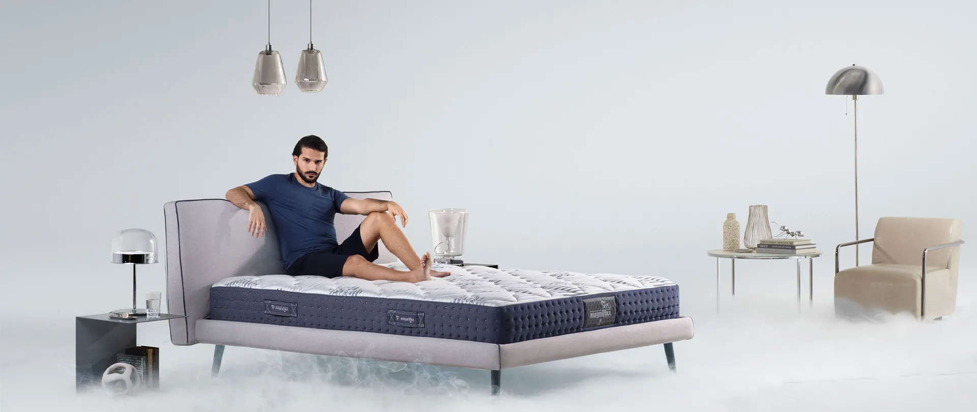 Materasso MagniCool Magniflex blu e bianco su letto imbottito, con un uomo sdraiato fra la nebbia fredda