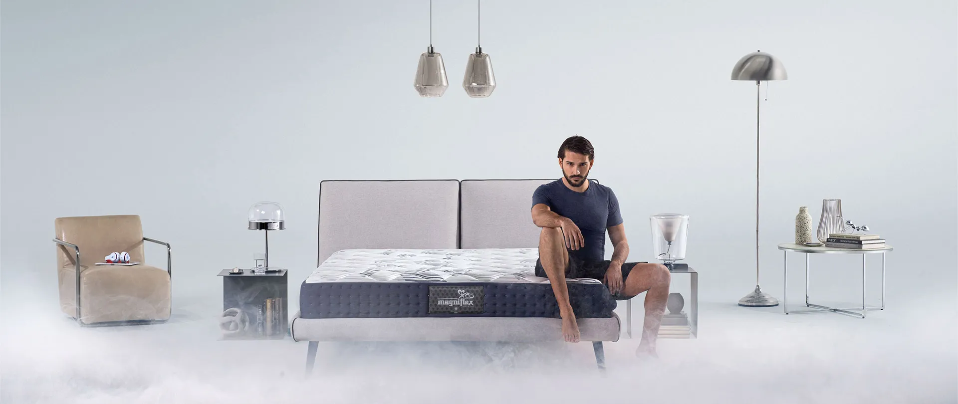 Materasso MagniCool Magniflex su letto con testiera chiara, un uomo seduto sul bordo in una stanza velata di nebbia