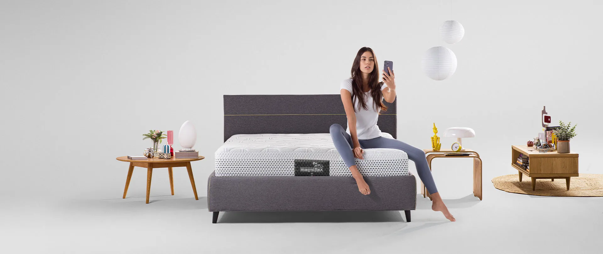 Materasso della collezione Classico Magniflex su letto grigio scuro, con una ragazza seduta che si scatta una foto