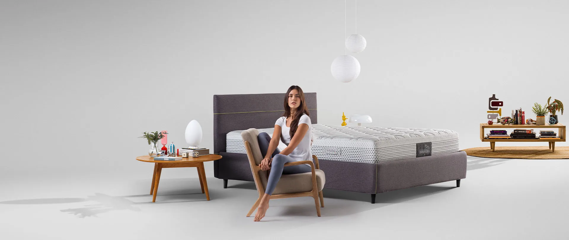 Materasso della collezione Classico Magniflex su letto grigio, con una ragazza seduta in poltrona davanti al letto