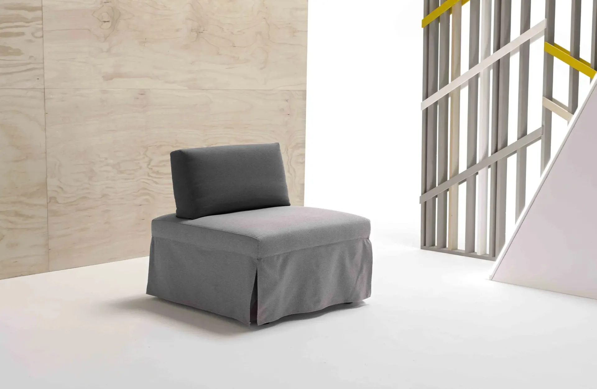 Poltrona letto Oplà Dienne grigia con schienale scuro davanti a una parete in legno